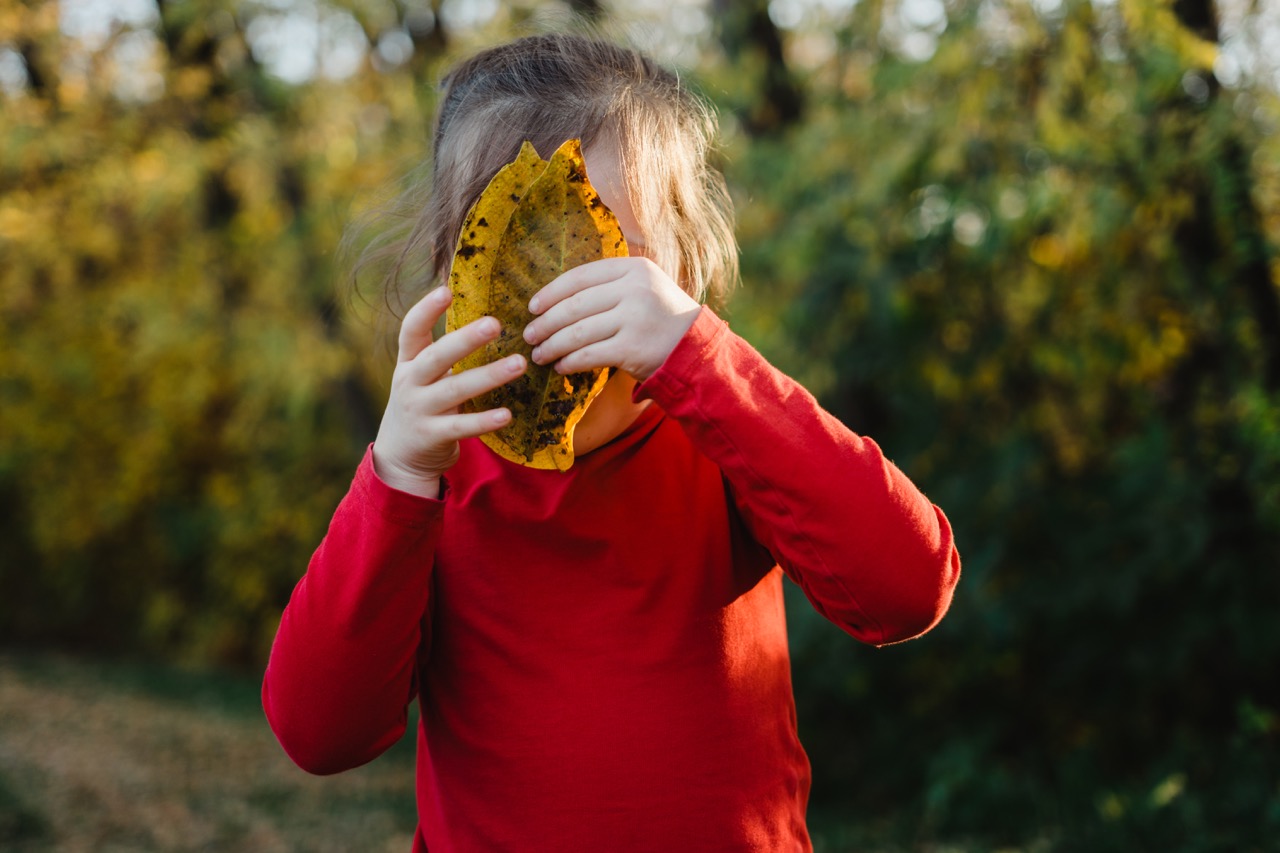 Child holding leaves in front of their face.