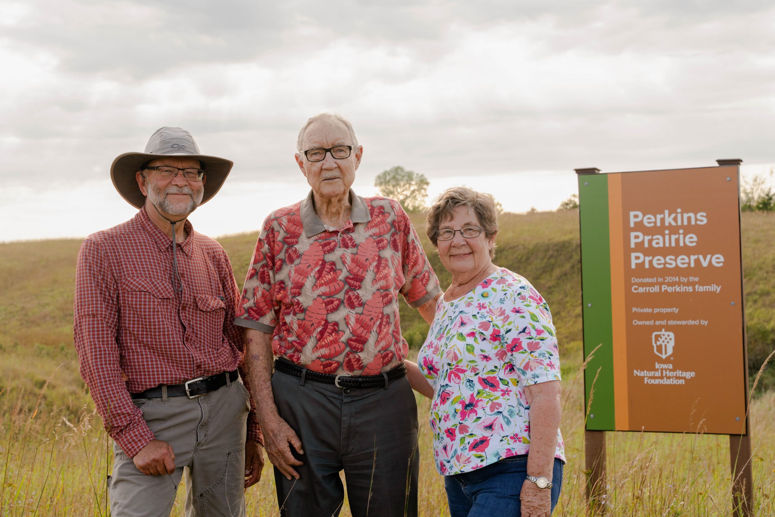 Jeff Jutting, Carroll Perkins and Karen Voge-Perkins stand by Perkins Prairie Preserve sign. 