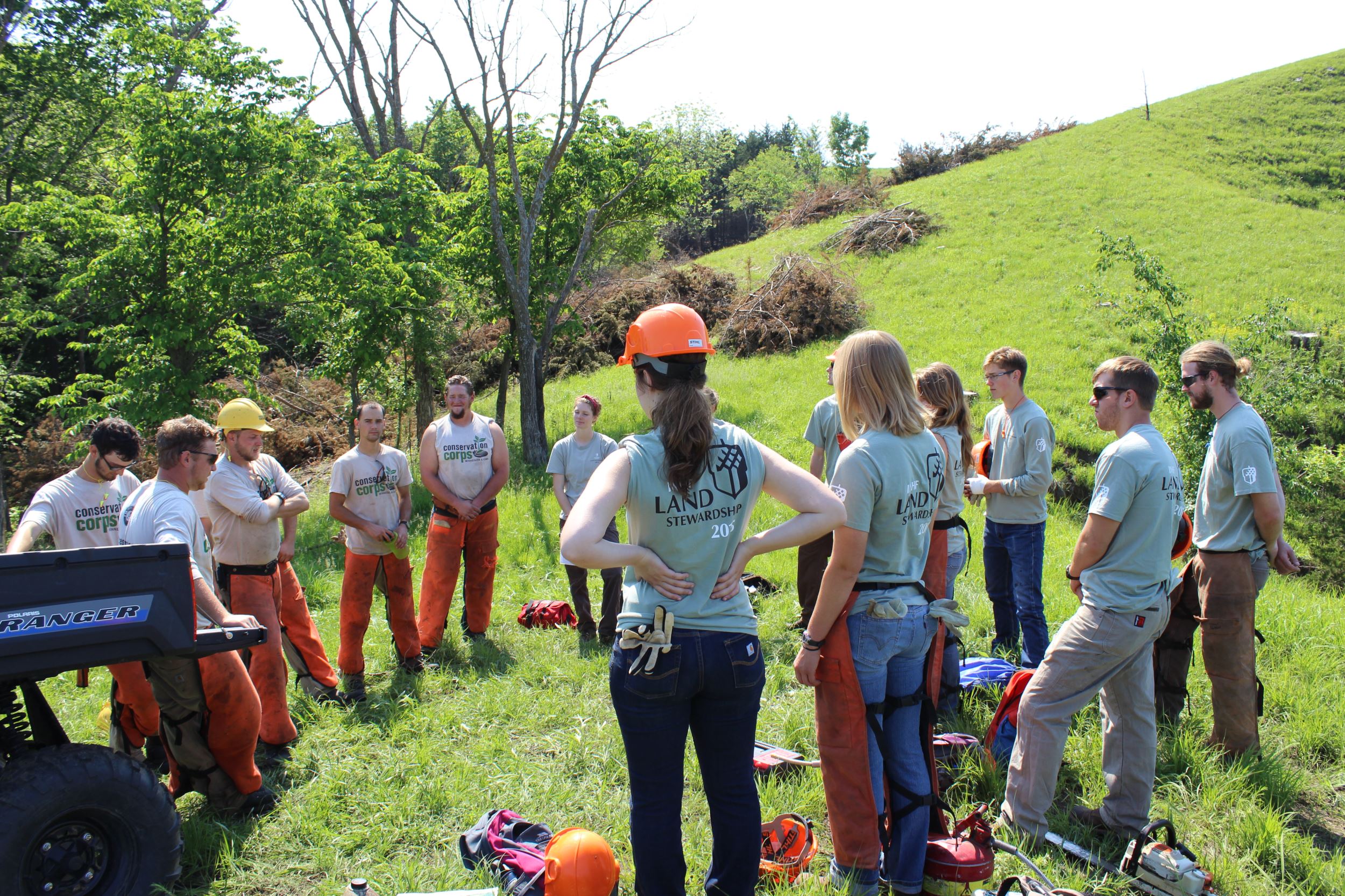 Conservation Corps Minnesota and Iowa staff and INHF interns stand in a cirlce at a work site.