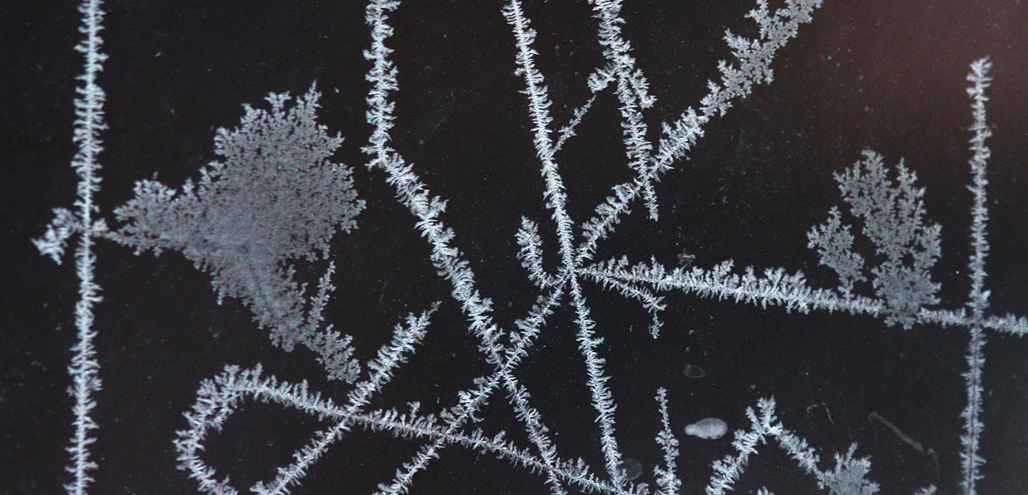 Everyone in cold climates has likely seen frost patterns on a window after a very cold night. It can take many different forms or shapes from lines to flowing flower-like designs. Formation occurs due to the difference in very cold air outside and moist humid air inside. Imperfections in the glass or on its surface such as dust, dirt, or scratches determine the form of the crystals. Higher humidity will also affect the thickness of the ice.